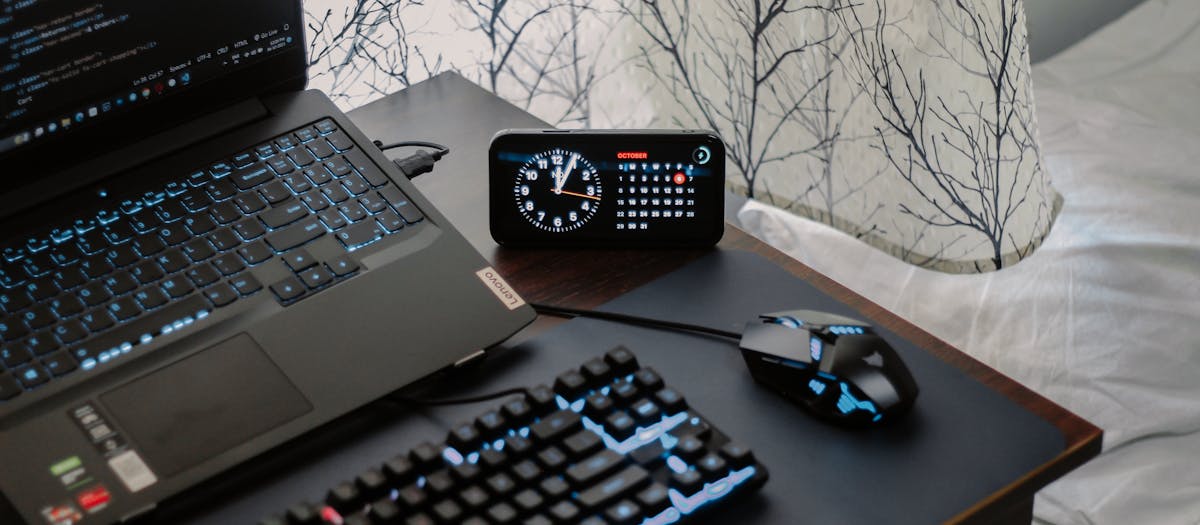 A modern workspace featuring a laptop, digital clock, gaming mouse, and keyboard, ideal for work and tech enthusiasts.